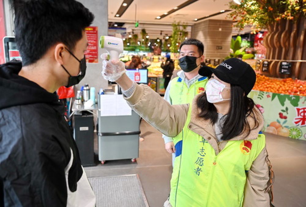 2月1日,青年志愿者吕抒婷(右)在福州市一家超市给购物者测量体温.