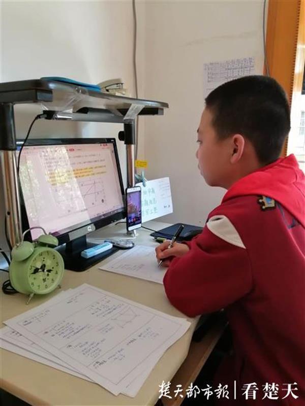 光谷二初703班学生刘博文在电脑上考试，一旁的手机在“监考”